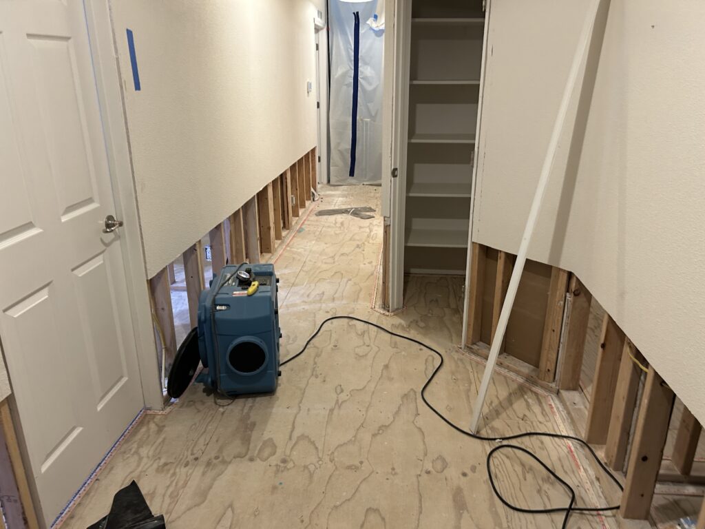 Hallway with baseboard and lower drywall removed and an air mover running