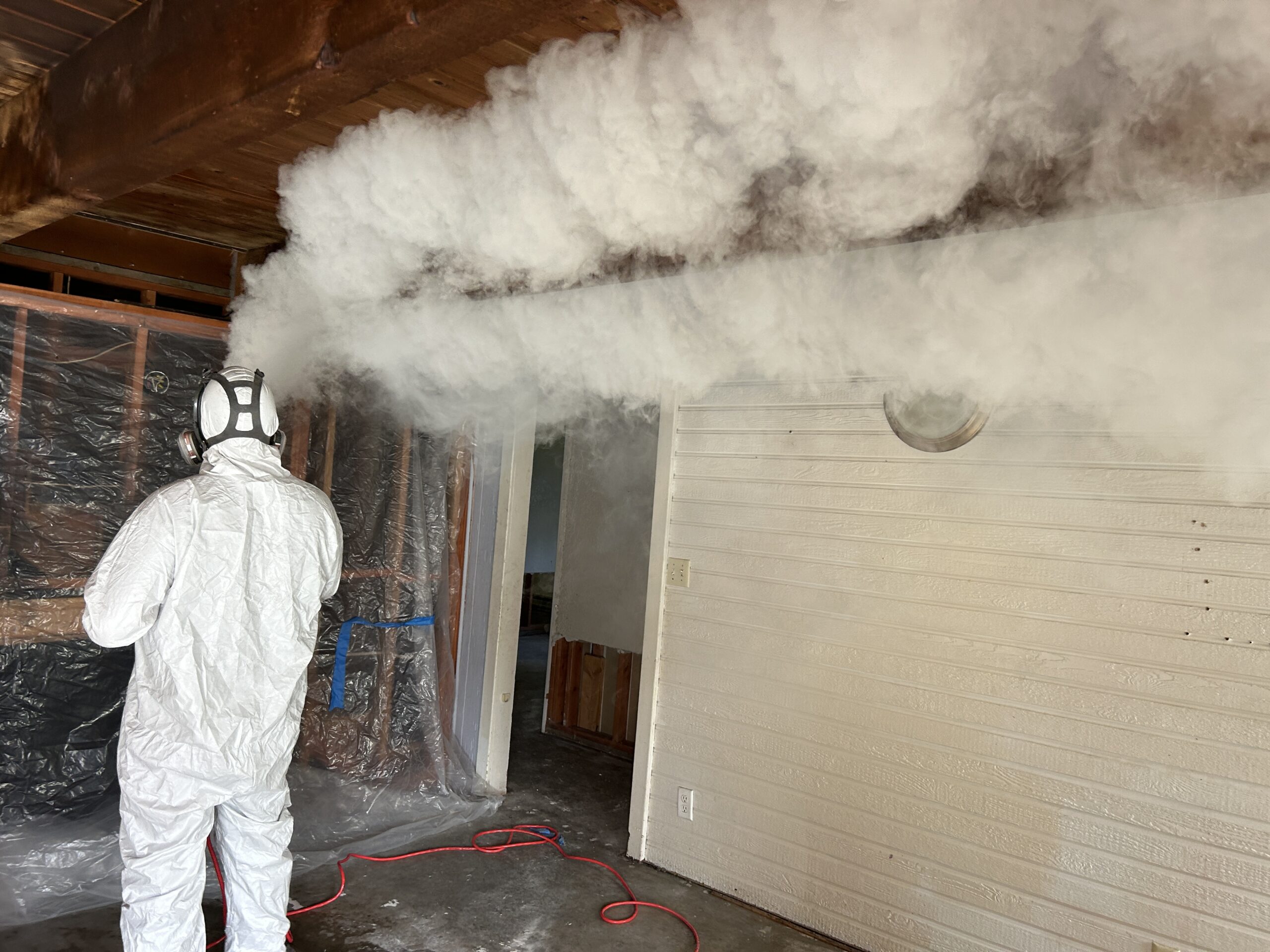 Technician in full protective equipment applying treatment in a stripped interior
