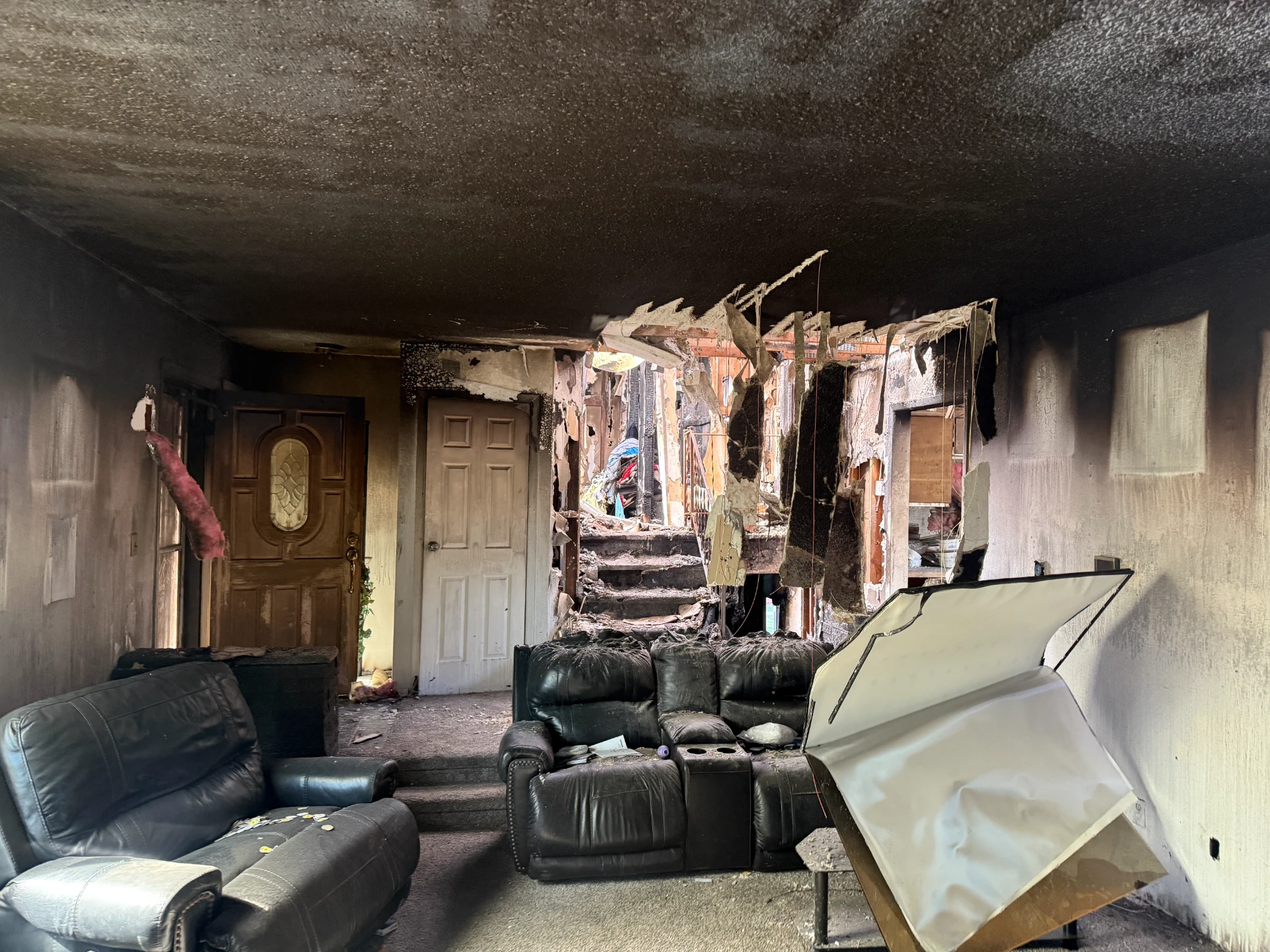 Soot-blackened interior of a house after a fire, with damaged furnishings