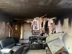 Soot-blackened interior of a house after a fire, with damaged furnishings