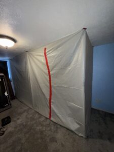 Plastic sheeting containment with a red zipper door built inside a bedroom to isolate the mold work area
