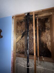 Bedroom wall opened to the studs, showing dark mold staining on the OSB sheathing, a black drain pipe, and the concrete foundation below