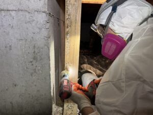 Technician in protective suit and respirator working in a confined crawlspace