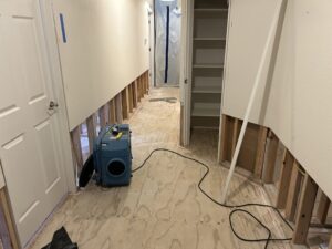 Hallway with baseboard and lower drywall removed and an air mover running